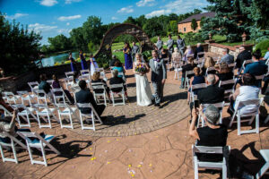 A wedding ceremony in an outdoor setting with rows of white chairs filled with guests.